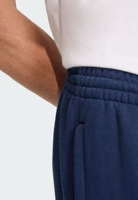 Calças de treino azul-marinho com cintura elástica, apresentando bolsos laterais e uma textura suave. Vista aproximada dos detalhes do tecido e da cintura.