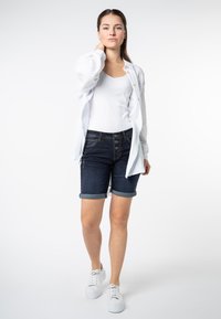 Witte, gestructureerde lange mouwen shirt, een witte aansluitende tanktop, donkere spijkerbroek met opgerolde mouwen, en witte sneakers. Vooraanzicht, neutrale achtergrond.