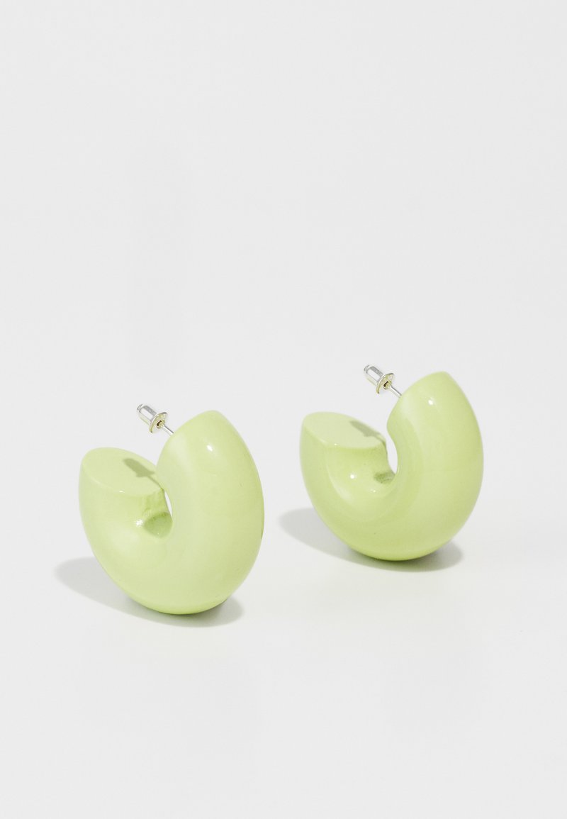 Zelené živicové náušnice v zakrivenom, abstraktnom tvare s lesklým povrchom. Dizajn obsahuje uchytenie na štupeľ pre jednoduché nosenie.