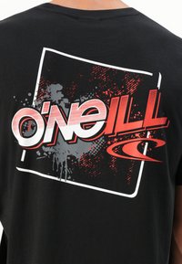Sort bomulds t-shirt med et stort grafik på ryggen i rød og hvid, med en sprøjteeffekt og ordet "O'Neill" iøjnefaldende præsenteret.