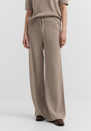 Beige ribbed knit wide-leg pants with drawstring waist worn with matching top and brown loafers, showing midsection and legs.
