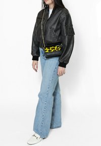 Giacca bomber in pelle nera con polsini a coste, jeans flare in denim chiaro e borsa a tracolla nera con motivo leopardato giallo.
