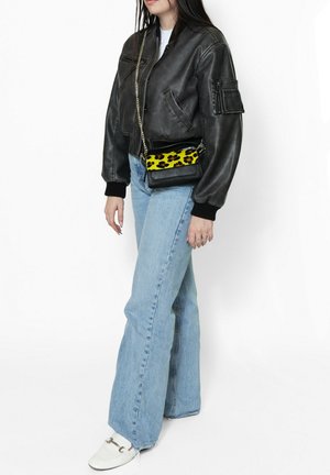 Schwarze Leder-Bomberjacke mit gerippten Bündchen, hellblaue, ausgestellte Jeans und eine schwarze Umhängetasche mit einem gelben Leopardenmuster.