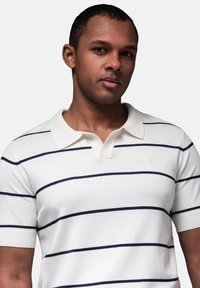 Vit randig polo skorta med marina horisontella ränder, klassisk krage, korta ärmar och en liten logotyp på vänster bröst.