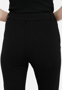 Pantaloni sartoriali neri realizzati in un tessuto liscio, caratterizzati da una vita aderente, tasche laterali e linee pulite, che enfatizzano una silhouette elegante.