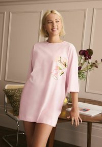Pink oversized t-shirt dress with a round neck, featuring a colorful cocktail graphic on the front. The fabric appears soft and smooth.