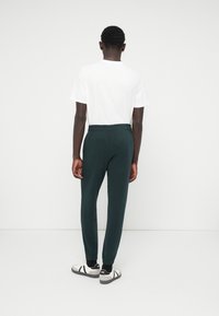 Pantalons de jogging pour hommes en vert foncé avec une taille élastique et des poignets élastiques, associés à un T-shirt blanc, vus de l'arrière, mettant en valeur un design simple.