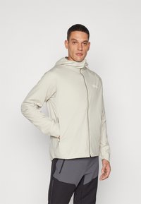 Lys beige zip-up jakke med hætte, som har en glat tekstur, minimalistisk design og et lille logo på brystet.