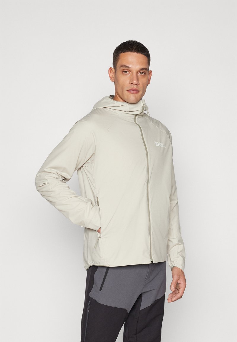 Lys beige zip-up jakke med hætte, som har en glat tekstur, minimalistisk design og et lille logo på brystet.