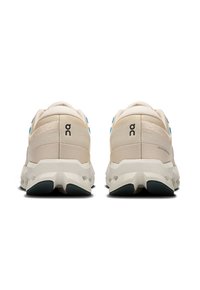 Scarpe da corsa beige con finitura testurizzata, dotate di accenti blu e un design della suola robusto. Logo visibile sul tallone.