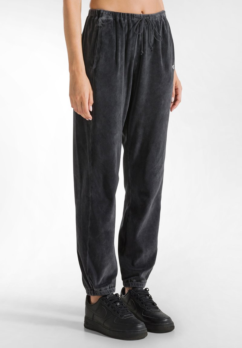Zwarte fluwelen sweatpants met elastische boorden, een trekkoord in de taille en zijzakken. Draagt met zwarte sneakers, wat een relaxte pasvorm laat zien.