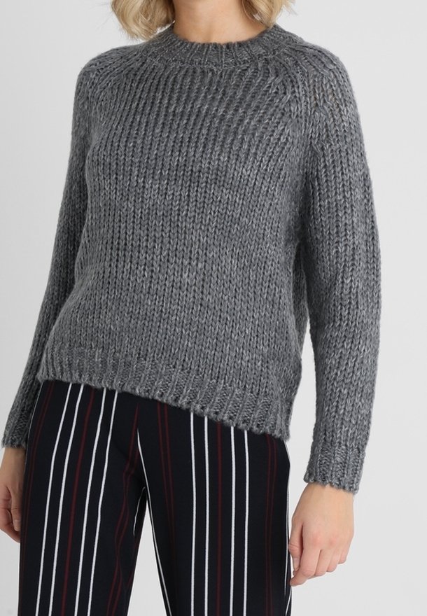 Pull gris en maille avec une texture côtelée, col rond et manches longues. La coupe est décontractée, associée à un pantalon rayé noir et blanc.