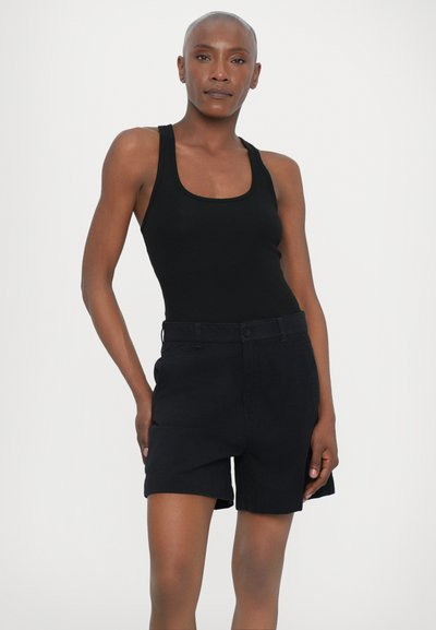 Svart, ribbet tanktopp kombinert med svarte skreddersydde shorts som har knappelukking. Stoffet ser glat ut med en strukturert passform.