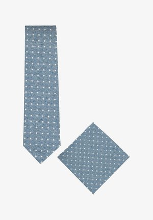 Blauwe stropdas en pochet set met witte polkadots en subtiele diagonale gestreepte textuur op een witte achtergrond.