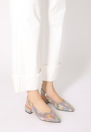 Colorful pointed-toe slingback heels with a geometric pattern, featuring a low block heel and a fabric texture, paired with white pants.