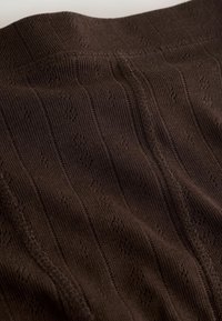 Gros plan sur un tissu tricoté marron foncé avec des motifs verticaux subtils et des coutures visibles.