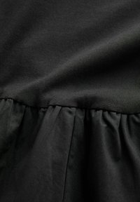 Tessuto di abito nero con una parte superiore liscia e una porzione inferiore arricciata. Il materiale sembra morbido con una consistenza uniforme in tutto.