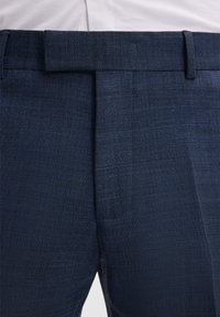 Pantaloni blu navy con tessuto texturizzato, caratterizzati da un fronte piatto, passanti per la cintura e una vestibilità su misura. Dettaglio di cuciture visibile in vita.