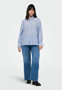 Light blue striped button-up shirt with long sleeves and tie accents, paired with flared blue jeans and black shoes.