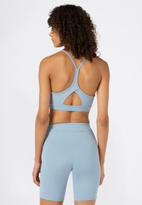 Sujeción deportiva de color azul claro con diseño de espalda tipo nadador y detalle de corte. Combinada con pantalones cortos de cintura alta a juego que presentan un logotipo en relieve.