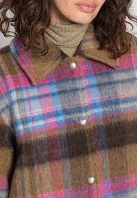 Abrigo de cuadros de lana que presenta una combinación de colores marrón, rosa, azul y gris. Tiene un cuello puntiagudo y botones de perla. Textura suave y peluda.