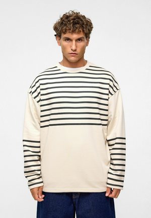 Beige shirt met lange mouwen en horizontale zwarte strepen, met een relaxte pasvorm en ronde halsontwerp. Zachte stof met een gladde textuur.