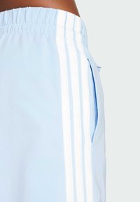 Pantalon de survêtement bleu clair avec une taille froncée, comportant deux rayures blanches sur le côté et une poche latérale pour le rangement. Tissu doux et agréable.