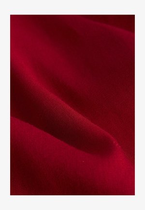 Punainen kangas, jossa on sileä pinta ja hienovarainen kiilto, esitettynä pehmeissä koukuissa, korostaen sen rikkaita värejä.