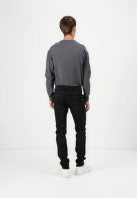 Black skinny jeans with a gray long-sleeve shirt, featuring straightforward design and clean lines. White sneakers complete the look.