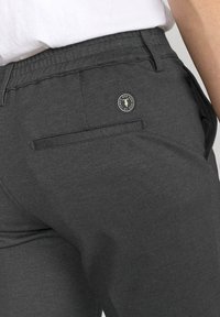 Donkergrijze broek met een gestructureerde stof, een achterzak met een horizontale opening en een logoaccent nabij de tailleband.