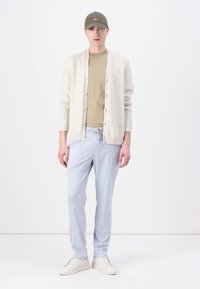 Cardigan tricotat într-o nuanță bej deschis, tricou oliv și pantaloni jogger de culoare albastru deschis. Adidașii albi completează ținuta, având o croială lejeră și butoane.