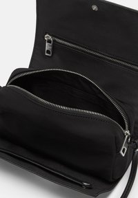 Czarna torba z tkaniny z główną komorą i zapinaną na zamek kieszenią, srebrnymi elementami i gładką fakturą w minimalistycznym designie.