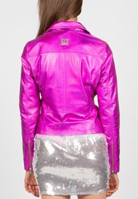 Kurtka ze skóry w kolorze fuksji z wyciętym kołnierzem, rękawami z zamkami oraz naszywką z logo na plecach. Połączona ze srebrną spódnicą cekinową.