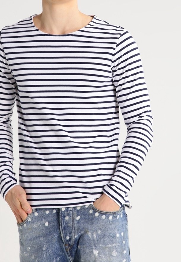 Langärmelige crew neck t-shirt, wit met marineblauwe horizontale strepen, gemaakt van katoen. Draagt met versleten spijkerbroek, handen in de zakken.