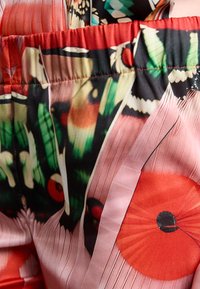 Tissu coloré et décoré de motifs floraux et circulaires en rouge, vert et noir. Texture douce avec un détail de taille élastique froncé.