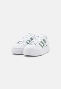 Witte sneakers met groene strepen, bovenwerk van textuurleer, ronde neus, gewatteerde kraag en een dikke witte rubberen zool.
