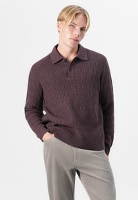 Knitted burgundy pullover with a textured pattern, front buttons, and a collared neck design, paired with gray corduroy pants.
