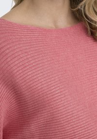 Rosa gerippter Strickoberteil mit Bootsausschnitt, das eine weiche Textur und einen subtilen Glanz aufweist, ohne zusätzliche Details oder Attachments präsentiert.