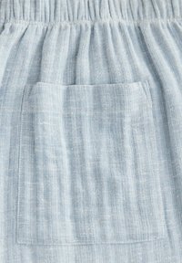 Light blue, textured fabric with vertical stripes. Features an elastic waistband and a single patch pocket. Soft and breathable material.