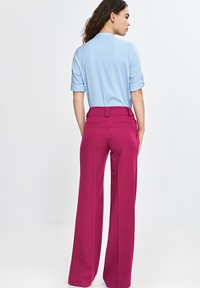 Jasnoniebieska koszula z podwiniętymi rękawami, w zestawieniu z spodniami o wysokim stanie i szerokich nogawkach w jaskrawym magencie. Gładki materiał z minimalnymi detalami.