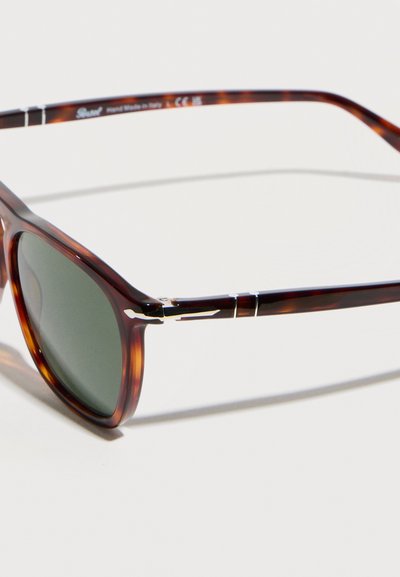 Ορθογώνια γυαλιά ηλίου με σχέδιο χελώνας, φακούς σκούρου πράσινου και λεπτές μεταλλικές λεπτομέρειες στο πλαίσιο και στα βραχίονες.