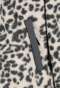 Leopard-print fleece fabric in beige and dark gray, featuring a smooth gray pull tab and a label of "SUBLEVEL CLOTHING."