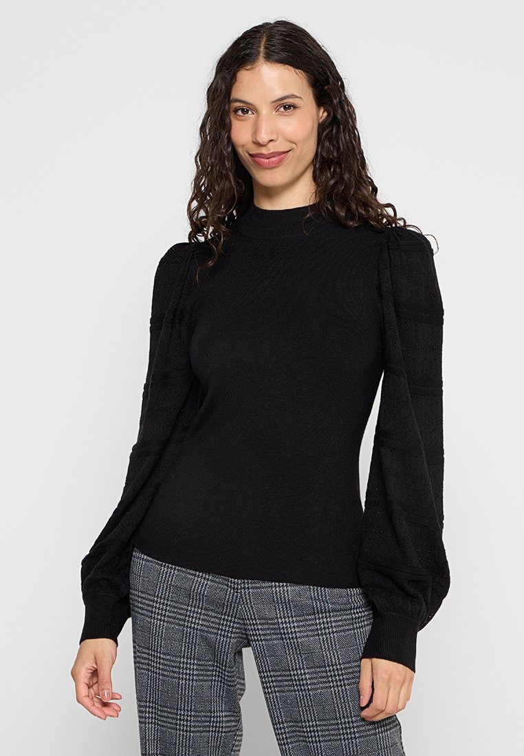 Pull noir avec des manches texturées et bouffantes et un col côtelé, associé à un pantalon à carreaux gris. Tissu en tricot lisse avec une silhouette ajustée.