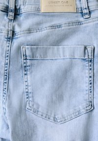 Light blue denim jeans with a stitched back pocket, featuring a leather label stating "STREET ONE" at the waistband. Smooth texture.