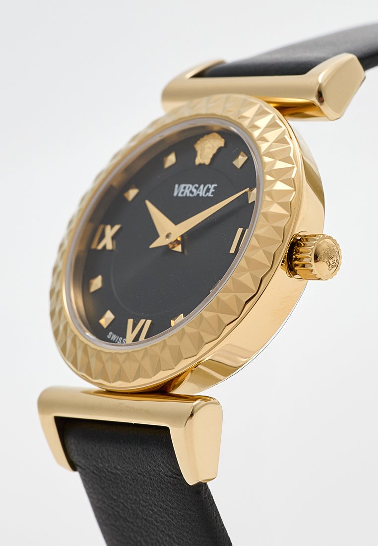 Montre dorée avec un cadran texturé, un cadran noir avec des chiffres romains, des aiguilles dorées et un bracelet en cuir noir. Logo en haut.