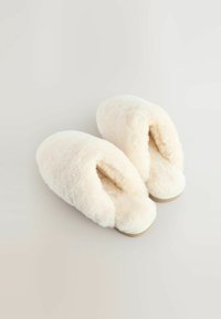 Kreminių spalvų šlepečių, pagamintų iš minkštos, pūkuotos medžiagos, dizainas su atvira nugarėle ir suapvalintu galiuku. Lygus padukas su minimaliais apdailos elementais.