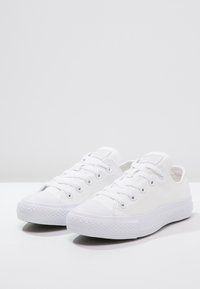 Weiße Leinenschuhe mit Gummikappen an den Zehen, flachen Schnürsenkeln und strukturierten Sohlen. Minimalistisches Design mit gesteppten Akzenten und Logo auf der Zunge.