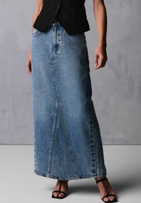 Denim maxi nederdel i lyseblå med lige snit, subtilt farveskift, to frontlommer og trykknaplukning langs siden.