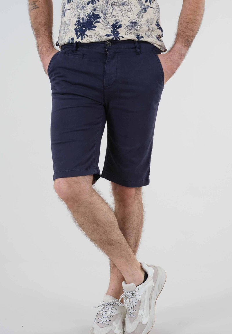 Shorts navy en coton avec une coupe droite, dotés de poches avant et de revers. Associés à des baskets légères.
