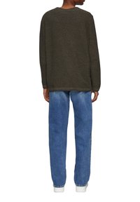 Dunkelgrüner Pullover mit lockerer Passform, langen Ärmeln und rundem Halsausschnitt, kombiniert mit blauem Denim-Jeans und weißen Sneakers.